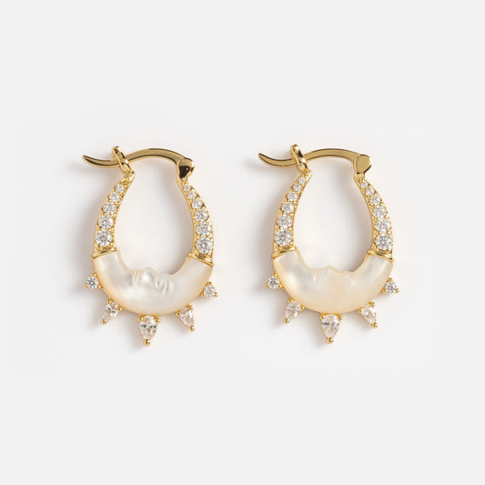 The Carved Moon Mother of Pearl Prophecy Earrings are gold hoops with white crystals, a mother-of-pearl inlay, and small triangular crystal accents hanging from the bottom edge.