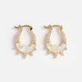 The Carved Moon Mother of Pearl Prophecy Earrings are gold hoops with white crystals, a mother-of-pearl inlay, and small triangular crystal accents hanging from the bottom edge.