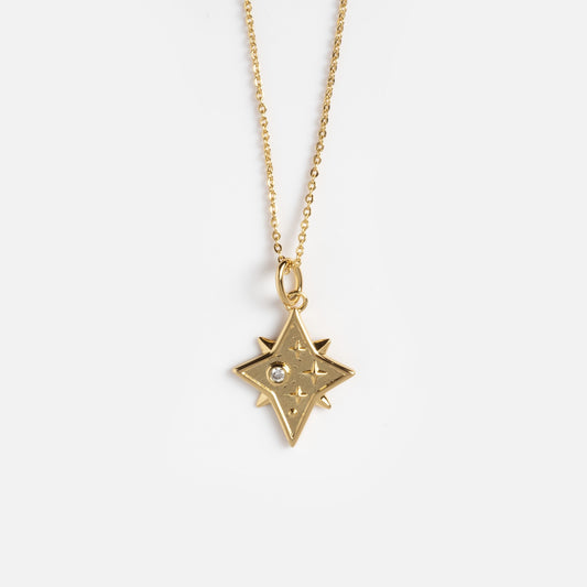 The Astral Guide Amulet Necklace features a thin gold chain with a star-shaped pendant, engraved rays, and a sparkling clear gemstone at its center, shown against a plain white background.