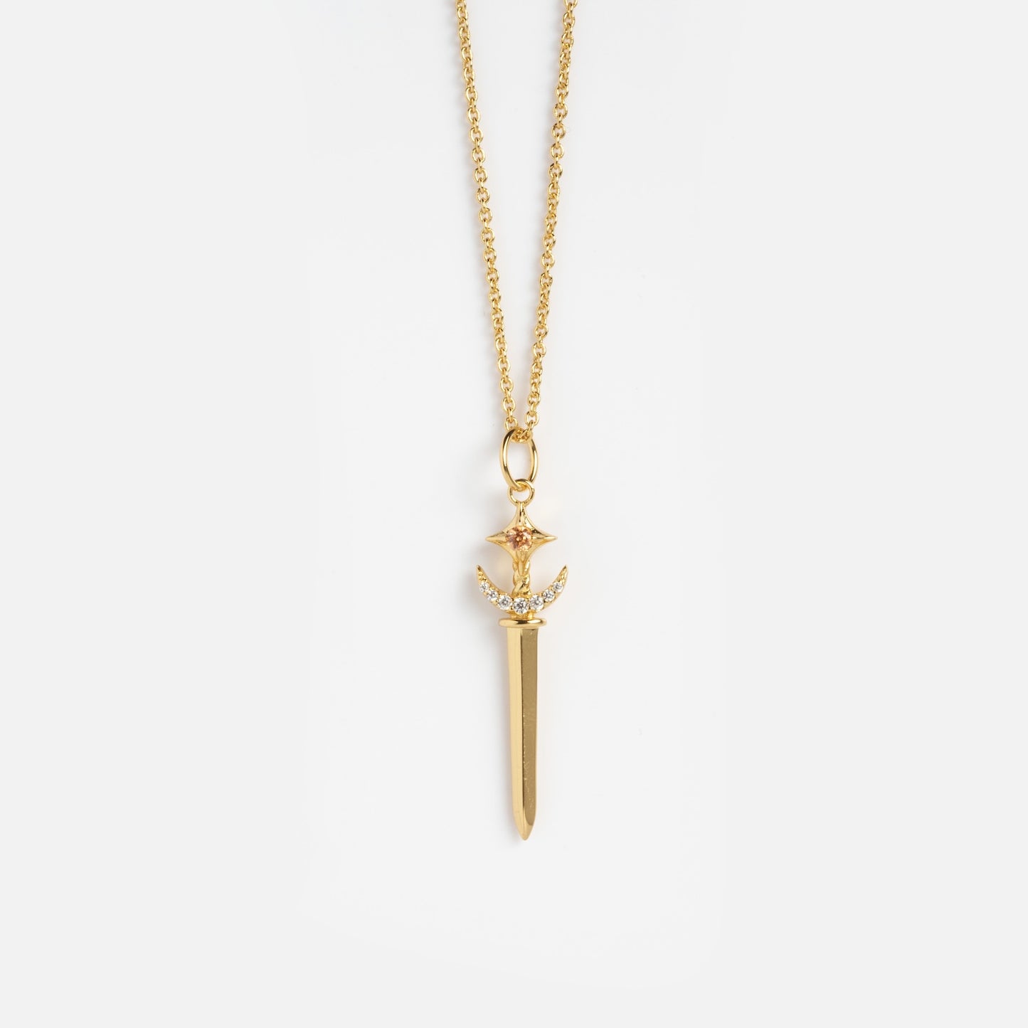 The Buffy Dagger Necklace features a gold sword-shaped pendant with a gemstone-studded hilt and intricate detailing, hanging from a fine gold chain and displayed against a white background.
