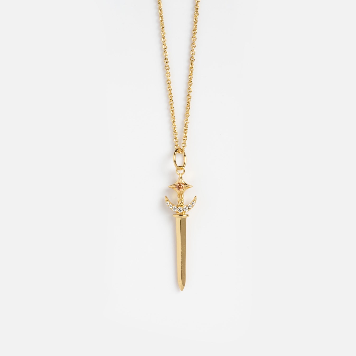 The Buffy Dagger Necklace features a gold sword-shaped pendant with a gemstone-studded hilt and intricate detailing, hanging from a fine gold chain and displayed against a white background.