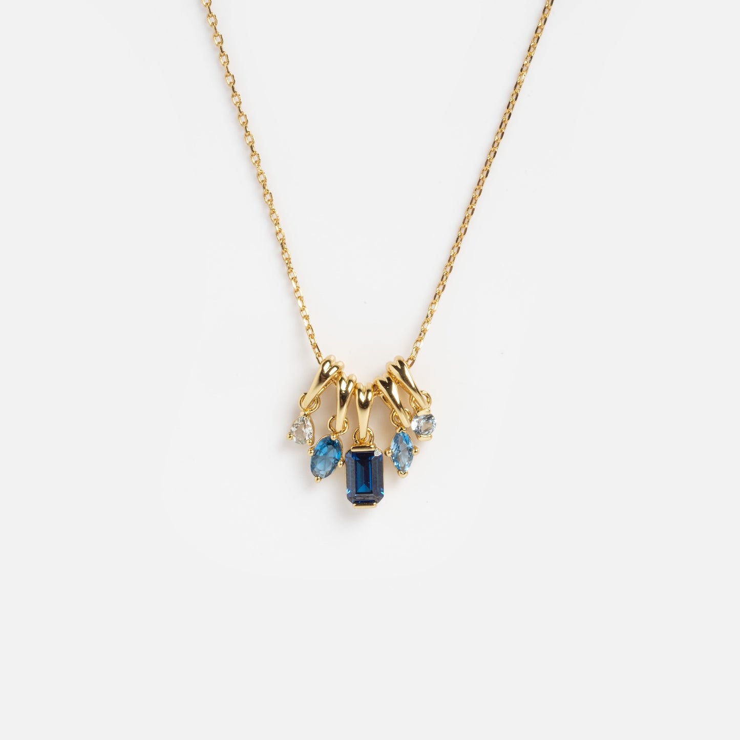The Shades of You Ombre Birthstone Charm Necklace features a gold chain with five blue and clear gemstone charms, including a central rectangular dark blue stone, displayed on a plain white background.