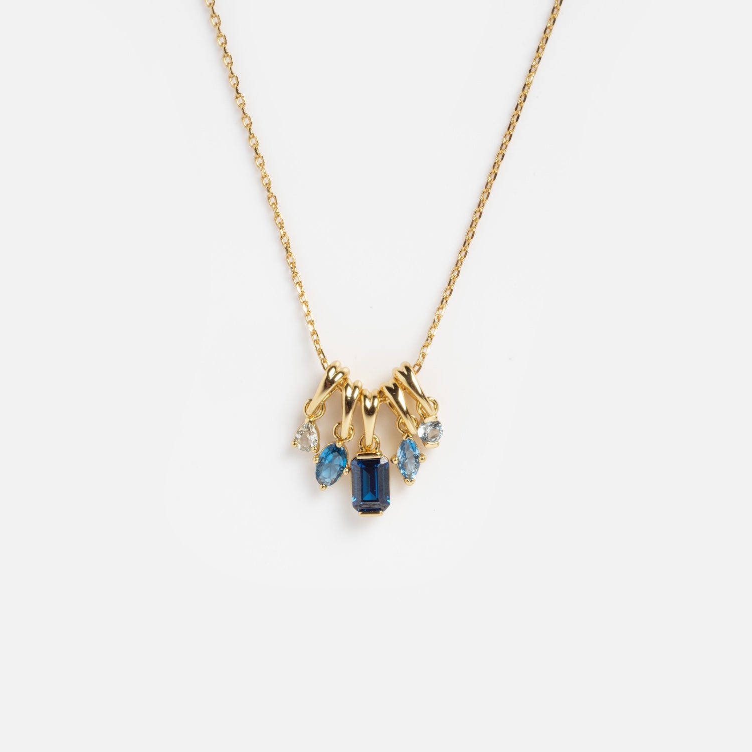The Shades of You Ombre Birthstone Charm Necklace features a gold chain with five blue and clear gemstone charms, including a central rectangular dark blue stone, displayed on a plain white background.