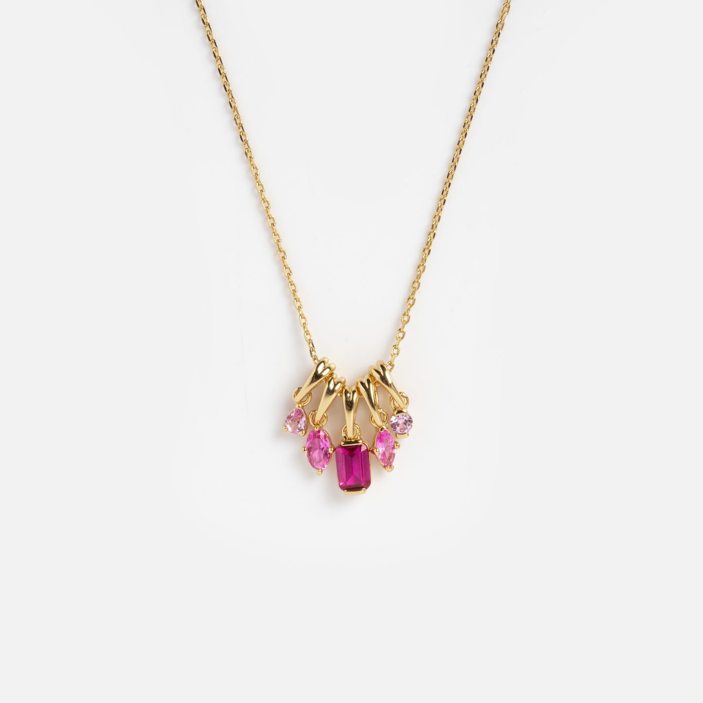 The Shades of You Ombre Birthstone Charm Necklace features five pink gemstones in different shapes and sizes as pendants, displayed on a gold chain against a plain white background.
