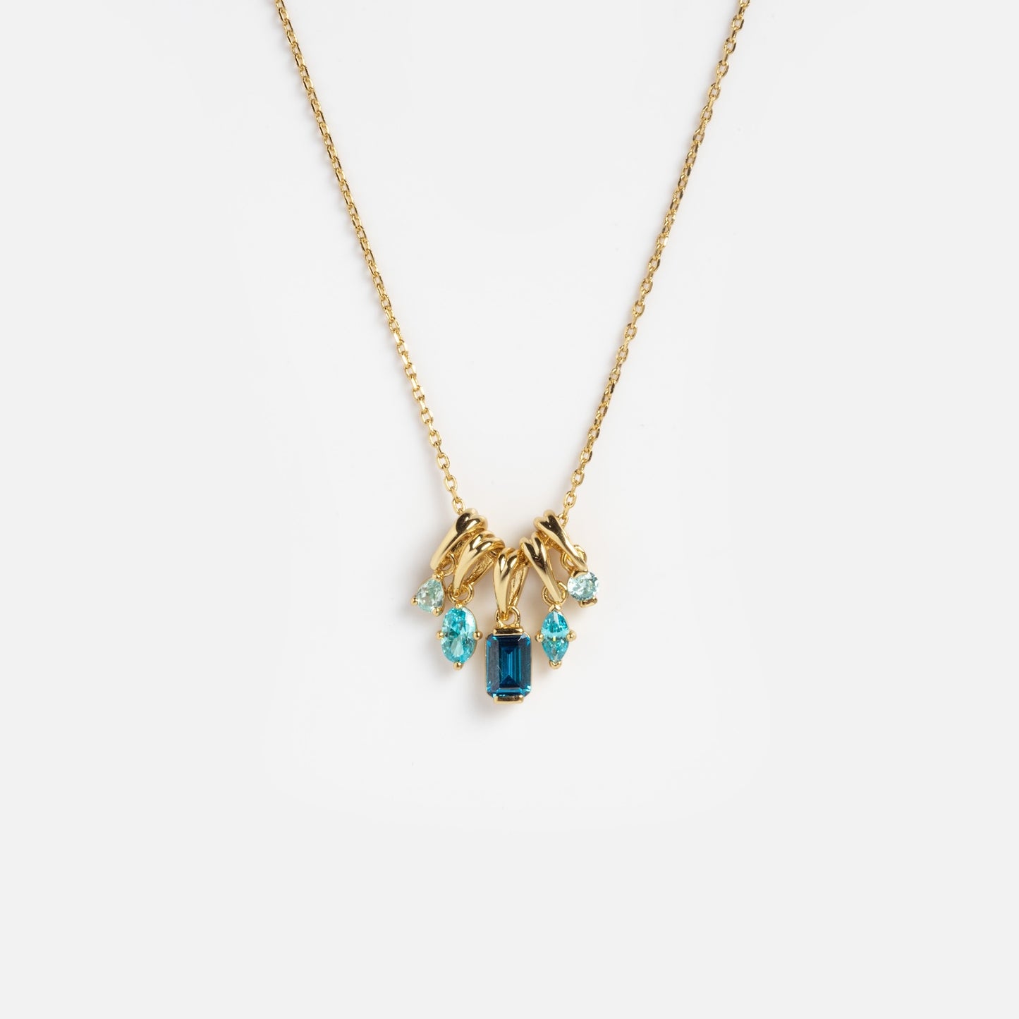 The Shades of You Ombre Birthstone Charm Necklace features five blue gemstones in different shapes, clustered on a delicate gold chain, displayed against a plain white background.