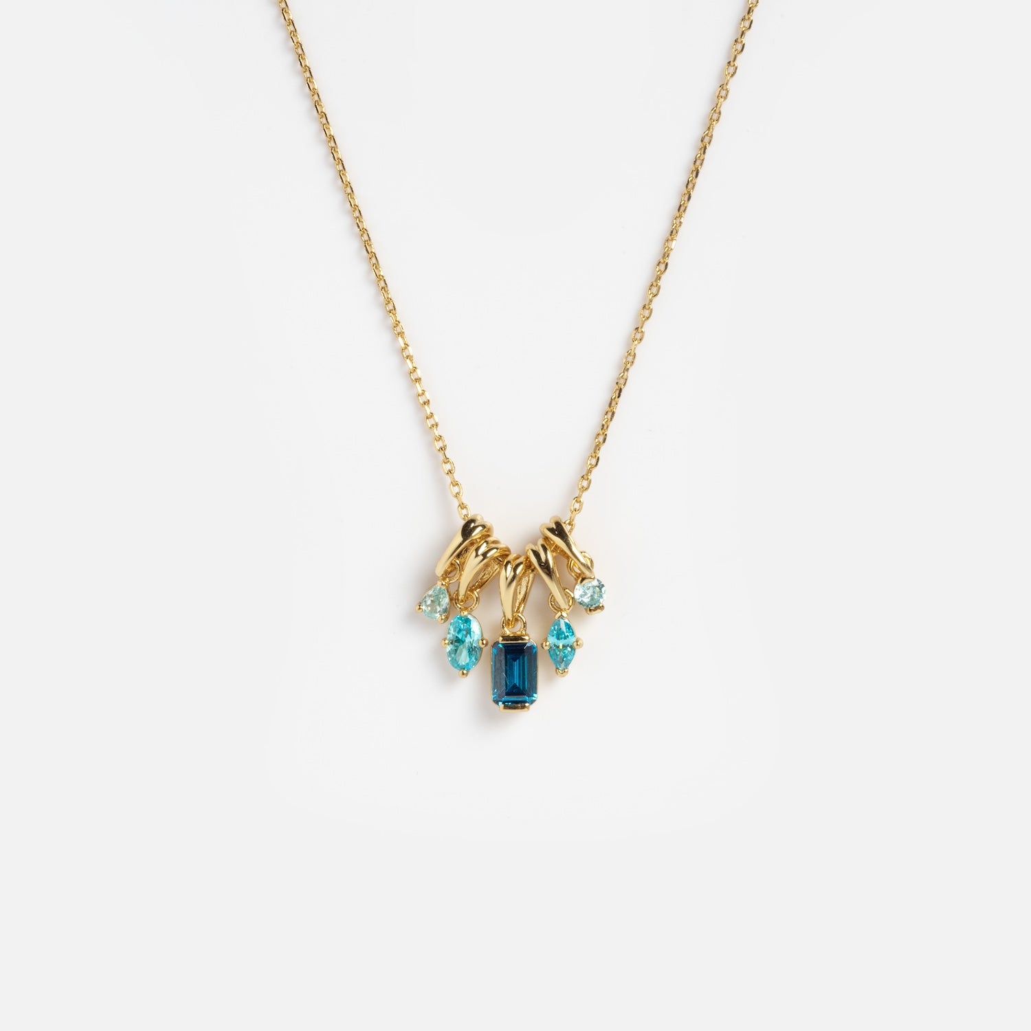 The Shades of You Ombre Birthstone Charm Necklace features five blue gemstones in different shapes, clustered on a delicate gold chain, displayed against a plain white background.