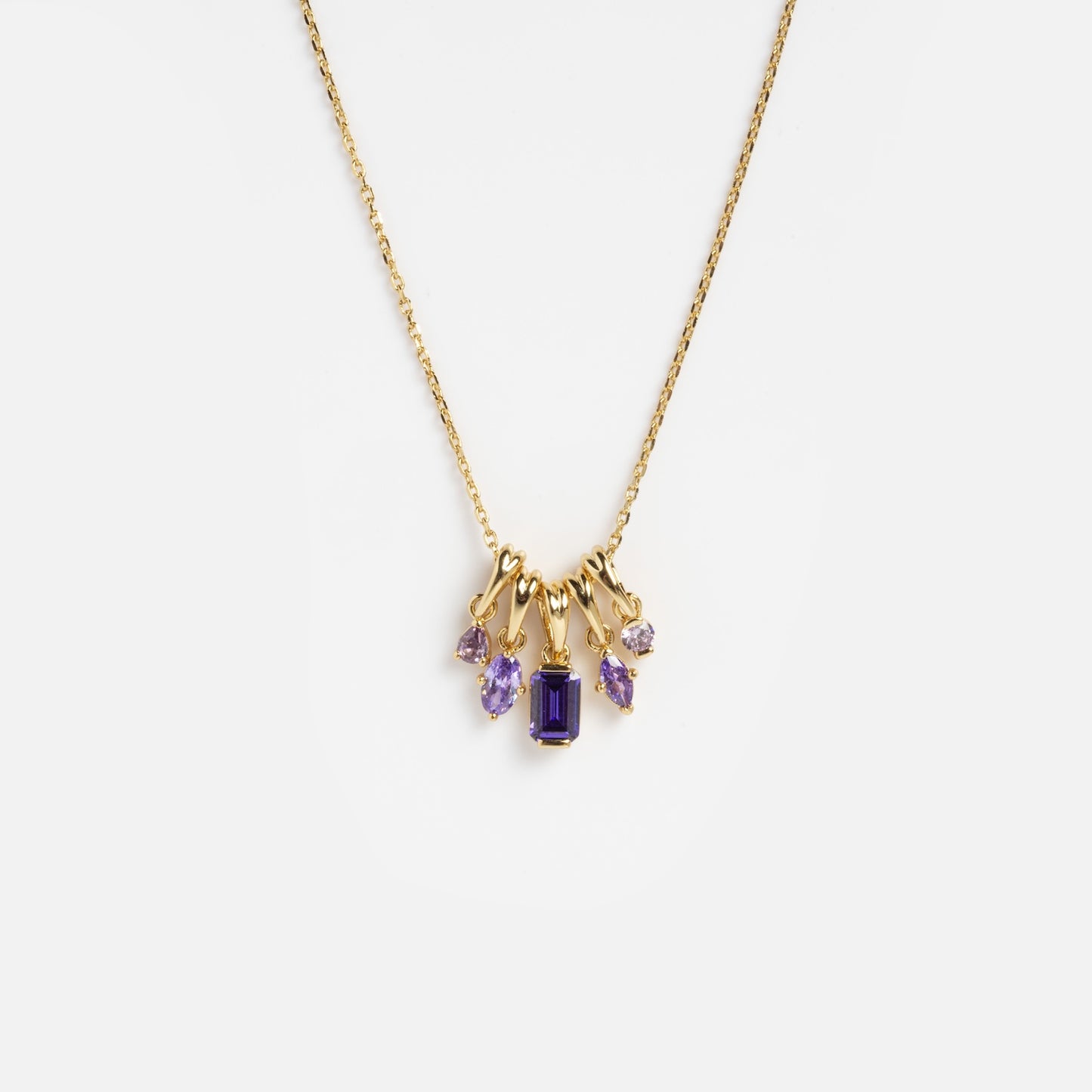 The Shades of You Ombre Birthstone Charm Necklace is a gold chain necklace with five purple gemstone pendants, featuring an emerald-cut center stone and four smaller, variously shaped stones, shown on a white background.