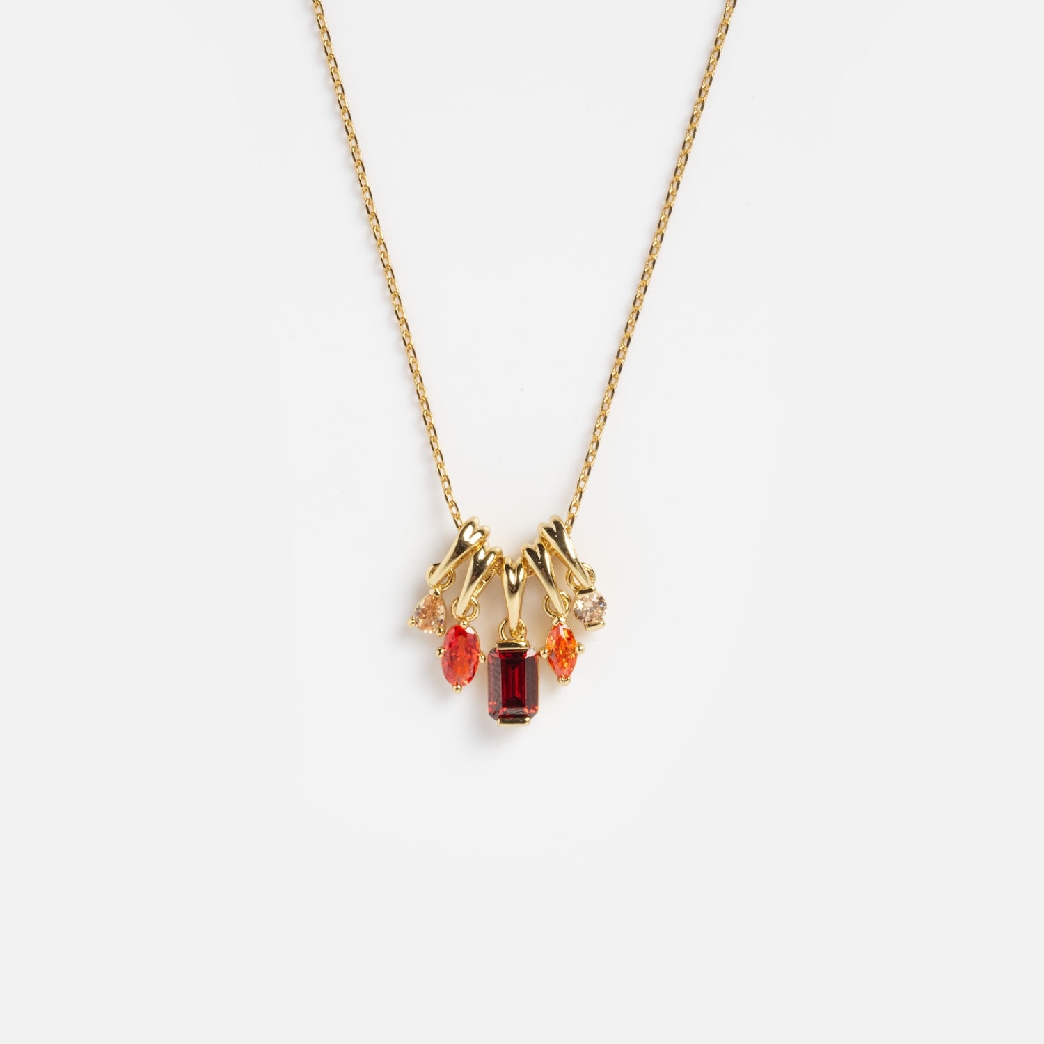 The Shades of You Ombre Birthstone Charm Necklace is a gold chain with five dangling gemstone charms in red, orange, and peach hues, each in unique shapes, shown on a plain white background.