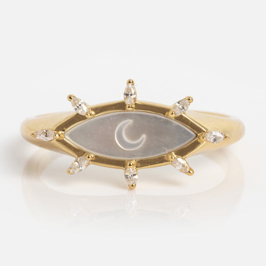 The Carved Moon Mother of Pearl Oracle Ring is a gold ring with an eye-shaped centerpiece, crescent moon detail, and eight marquise-cut diamonds around the edge resembling rays or eyelashes.