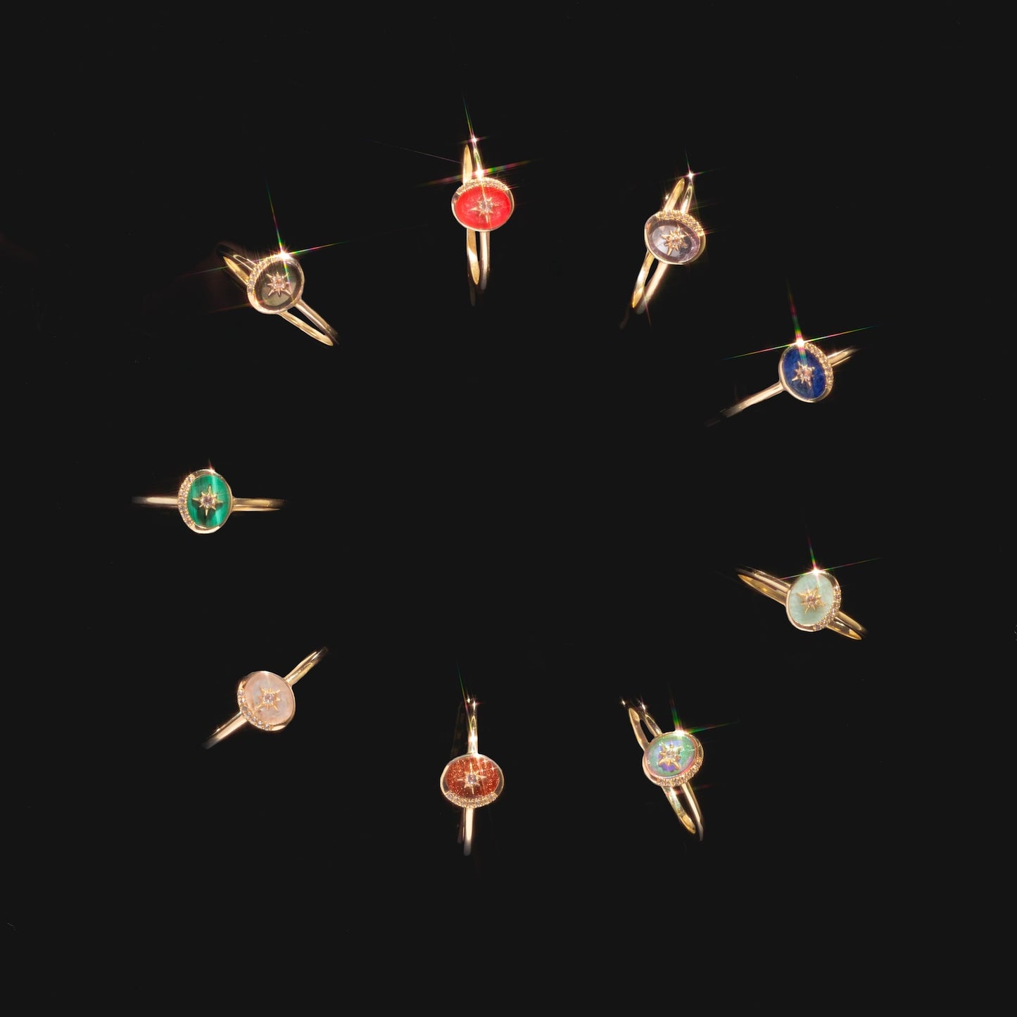 Ten Solid Gold Crystal Crescent Moon Rings for Manifestation, each with a distinct colored gemstone—red, blue, green, and clear crystals—are arranged in a circle on a black background.