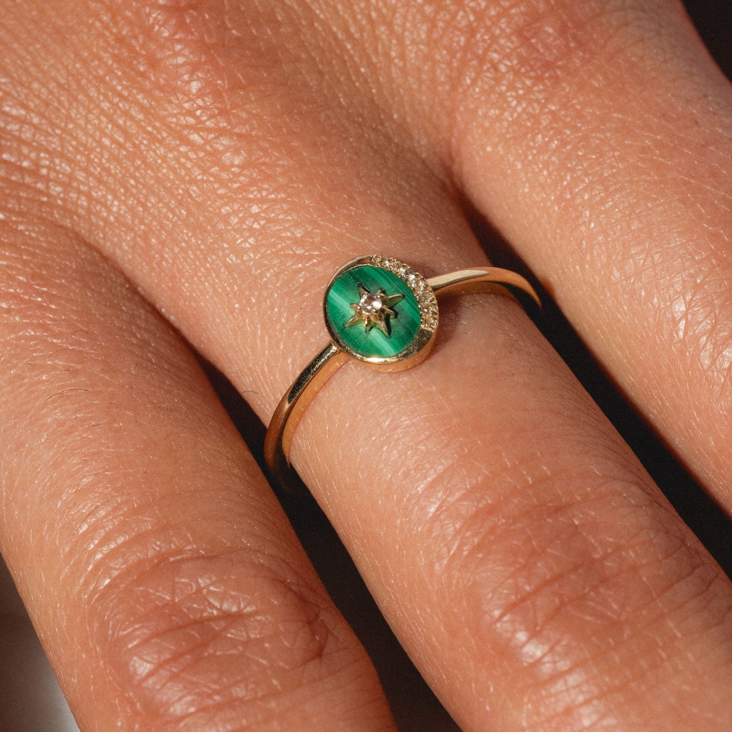 A close-up of a hand wearing the Solid Gold Crystal Crescent Moon Ring for Manifestation, featuring a green oval stone centerpiece, delicate star-shaped detail, and tiny gemstone—an ideal ring for manifestation.