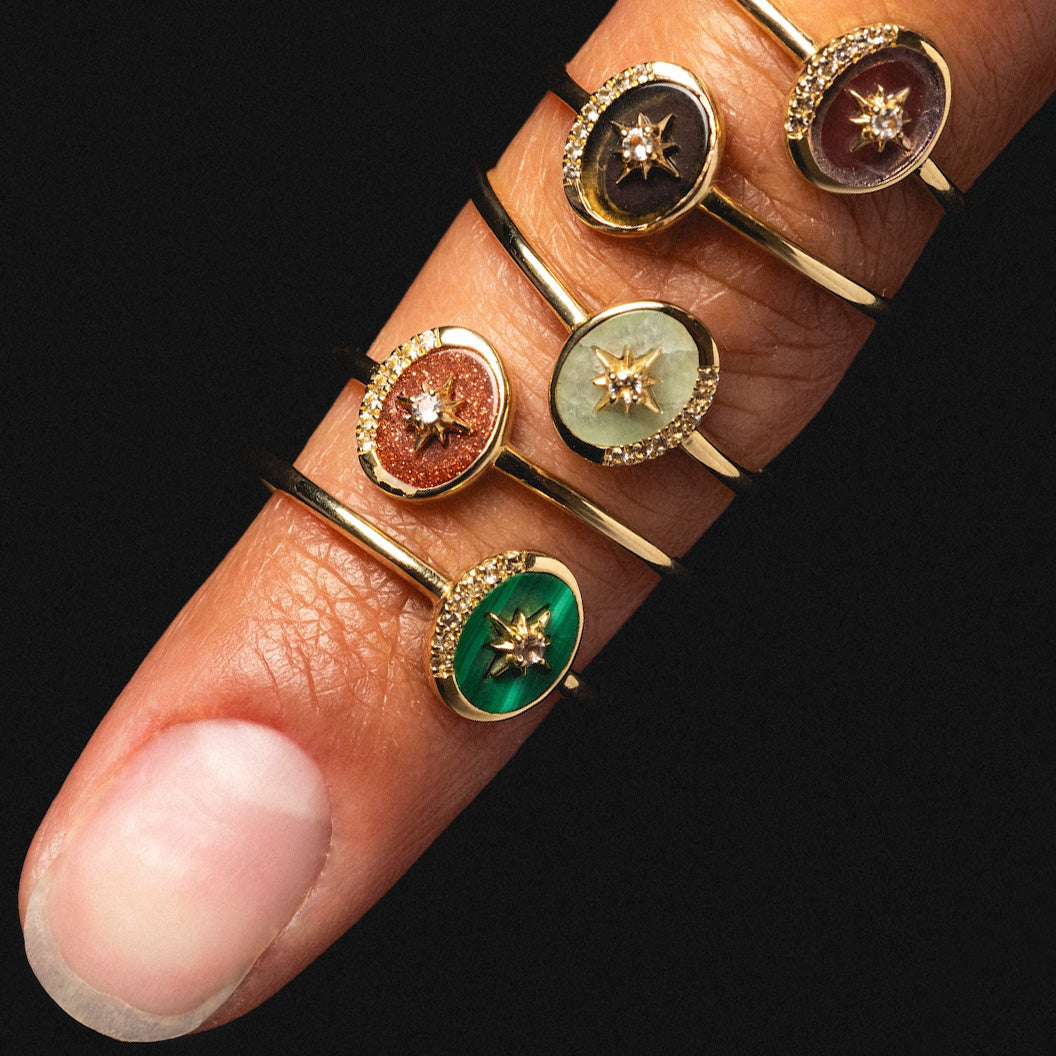 A close-up of a finger showcases five Solid Gold Crystal Crescent Moon Rings for Manifestation, each featuring a unique colored natural crystal oval gemstone and a central star-shaped detail, stacked stylishly along the finger.