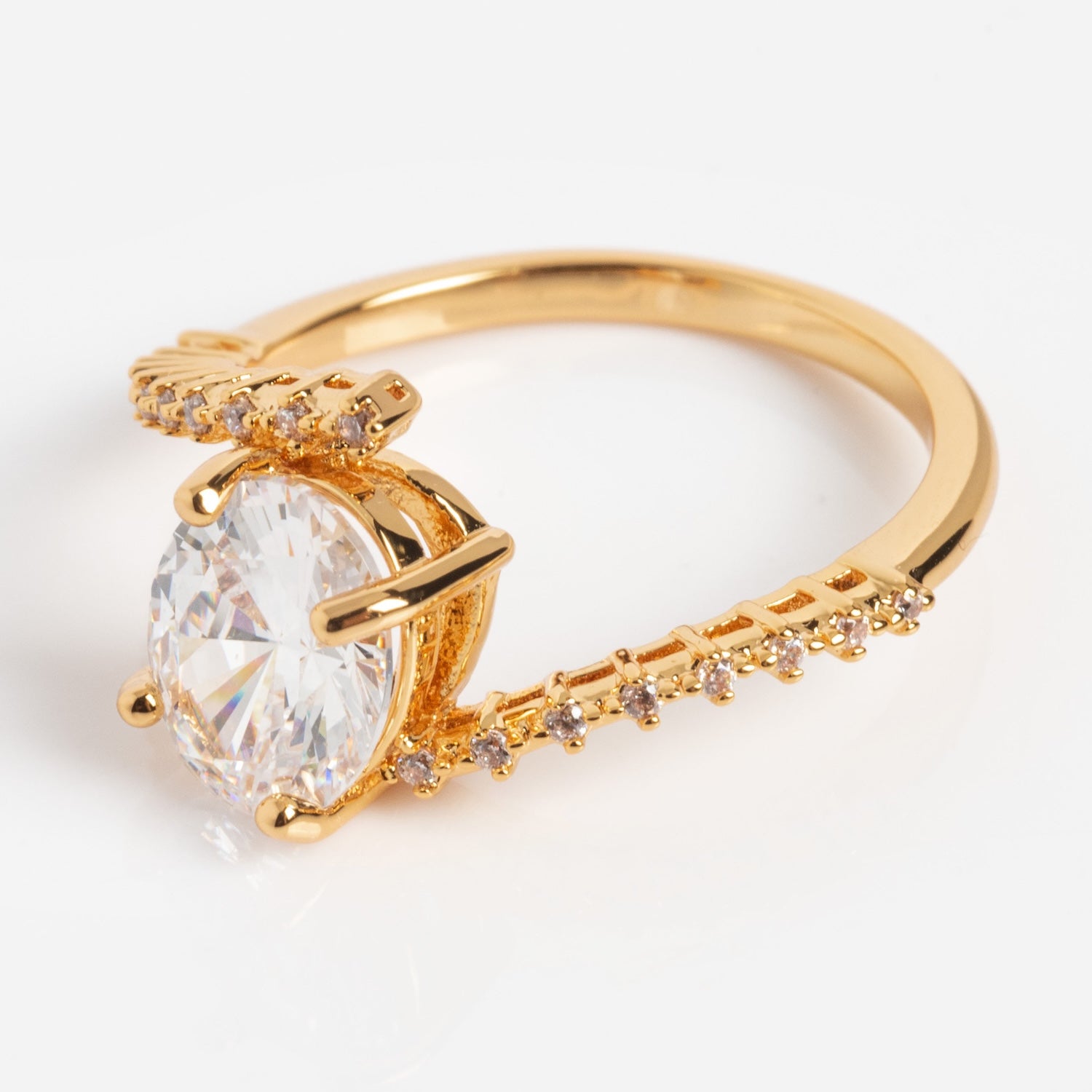The Tilted CZ Ring is a gold band featuring a large oval-cut clear cubic zirconia at the center, accented with small round stones along the band and displayed on a white background.