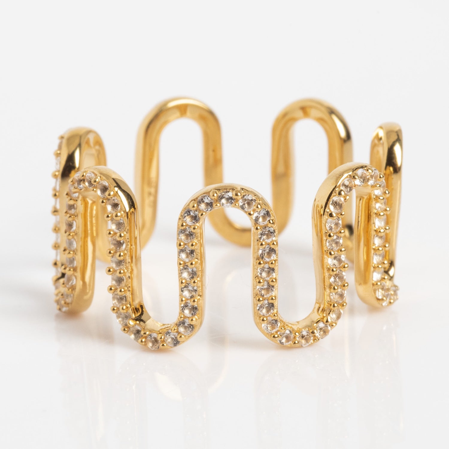 The Curtain Call Cascade Ring is a gold ring featuring a wavy, zigzag design with sparkling white stones along the curves, displayed on a white background.