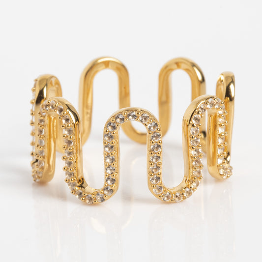 The Curtain Call Cascade Ring is a gold ring featuring a wavy, zigzag design with sparkling white stones along the curves, displayed on a white background.