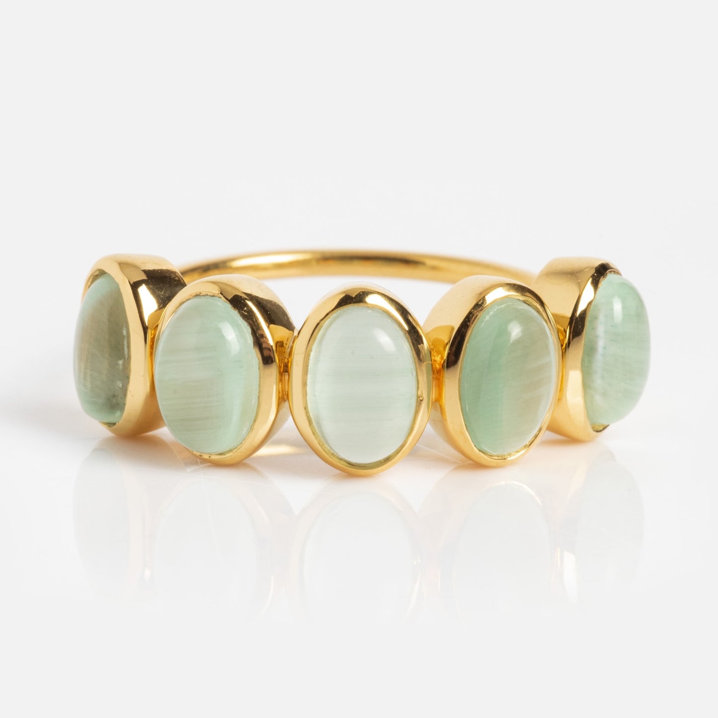 The Sky Blue Cats Eye Flow Ring showcases five oval, pale sky blue cat’s eye gemstones in a row, set on a gold band and displayed against a white background.