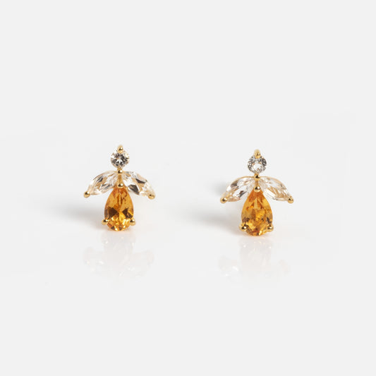 The Jazz Age Citrine Studs are gold earrings shaped like angels, with a yellow teardrop gem for the body, two clear marquise stones as wings, and a round clear gem as the head, all set against a white background.