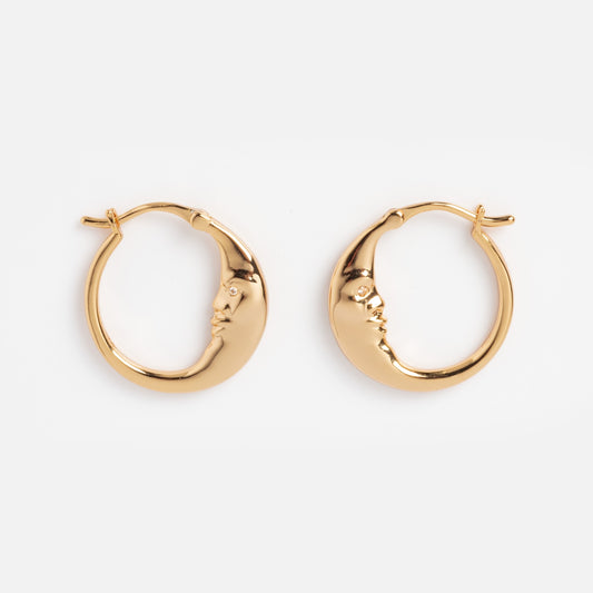 Petite Luna Hoops: Gold crescent moon earrings with sculpted closed-eye faces on each curve, displayed on a plain white background.