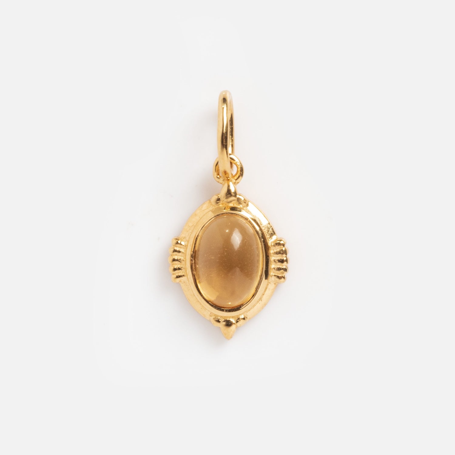 The Vintage Inspired Pendant Charm features an oval-shaped gold design with a smooth amber stone, decorative accents, and a small top loop—perfect for fans of Period Piece jewelry.