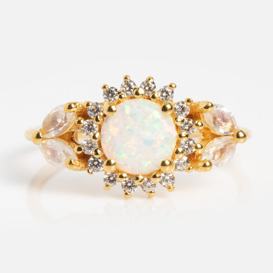 The Opal and Diamond Sunflower Queen Ring showcases a round opal center stone, haloed by clear diamonds with marquise-shaped accents, all set in gold against a white background.