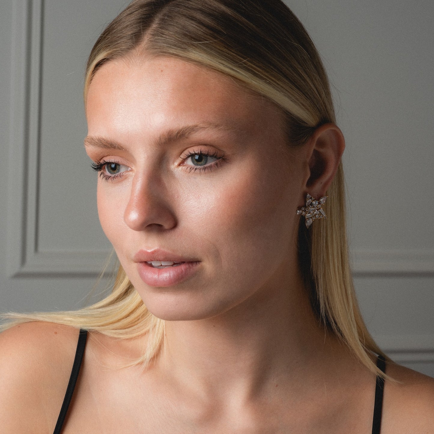 A woman with straight blonde hair wears a black spaghetti strap top and the Debut Star Stud Earrings, looking slightly to the side against a neutral background.