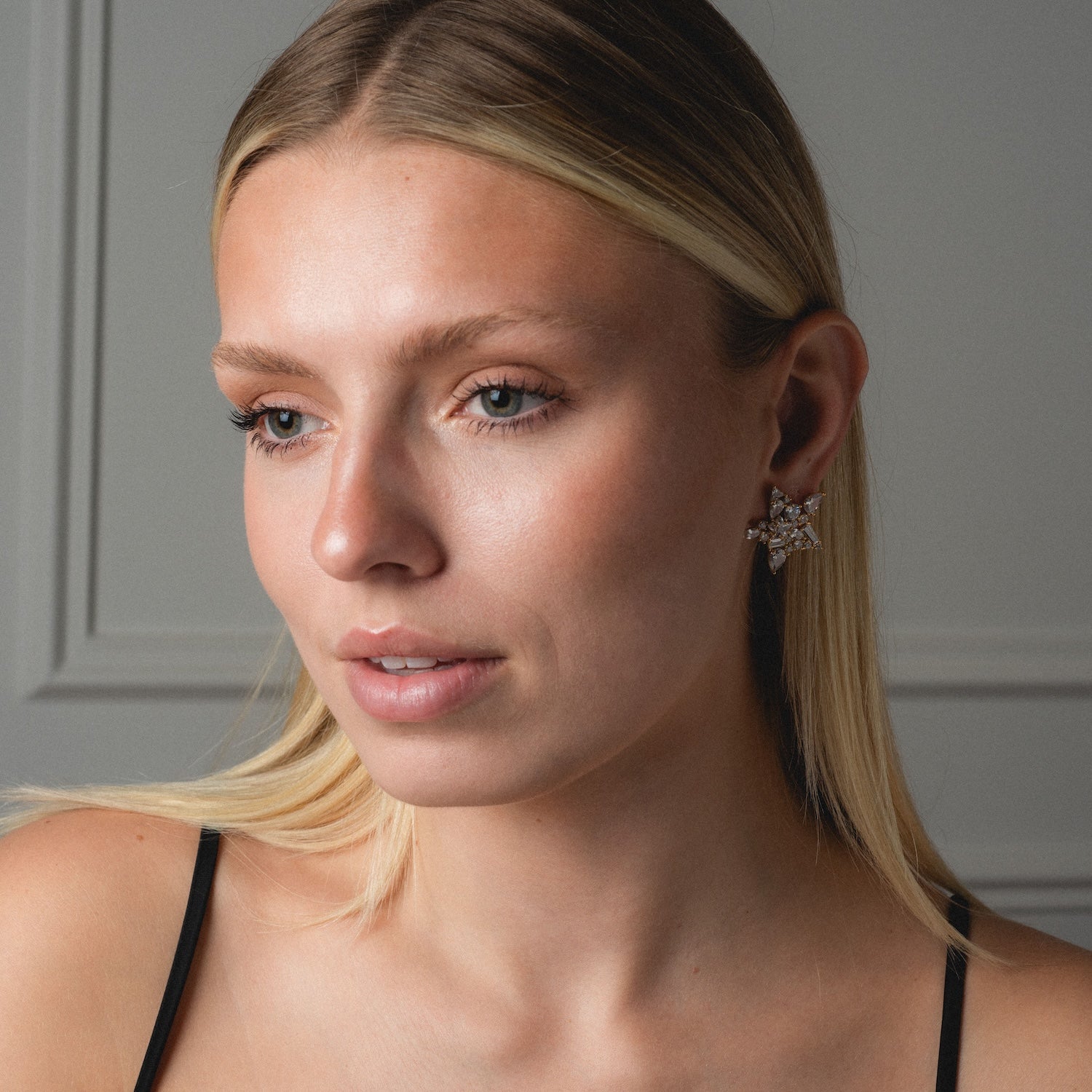 A woman with straight blonde hair wears a black spaghetti strap top and the Debut Star Stud Earrings, looking slightly to the side against a neutral background.