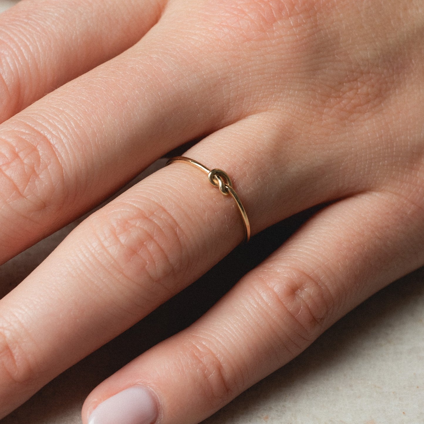 A close-up of a hand wearing the Solid Gold Simple Knot Ring in 10k yellow gold, delicately resting on a light surface. The nails are neatly trimmed and natural.