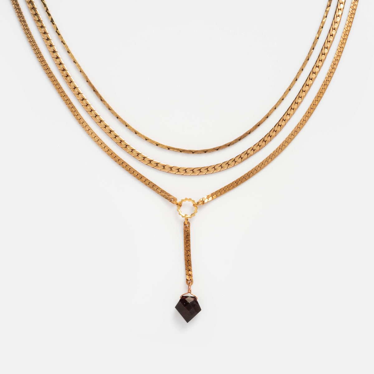 The Palmer Gemstone Necklace features three recycled brass chains with a gold layer and a central ring, showcasing a single black geometric pendant on the middle chain.
