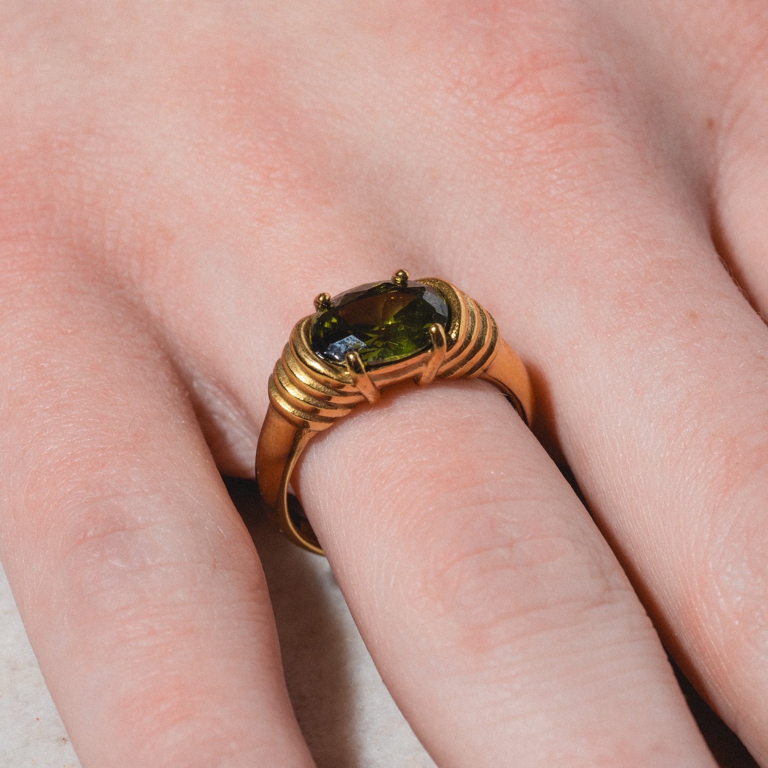 A close-up of a hand wearing the Stone Statement Ring—a gold band with a rectangular dark green gemstone and decorative ridges flanking the stone.