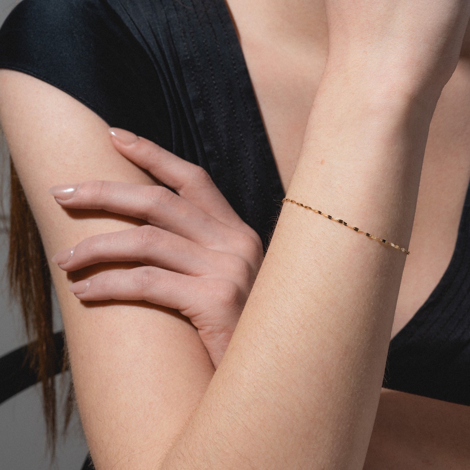 A woman in a black top crosses her arms, showcasing the Solid Gold Bold Sparkle Link Chain Bracelet on her wrist. Her nails are naturally polished, and the neutral background is blurred.