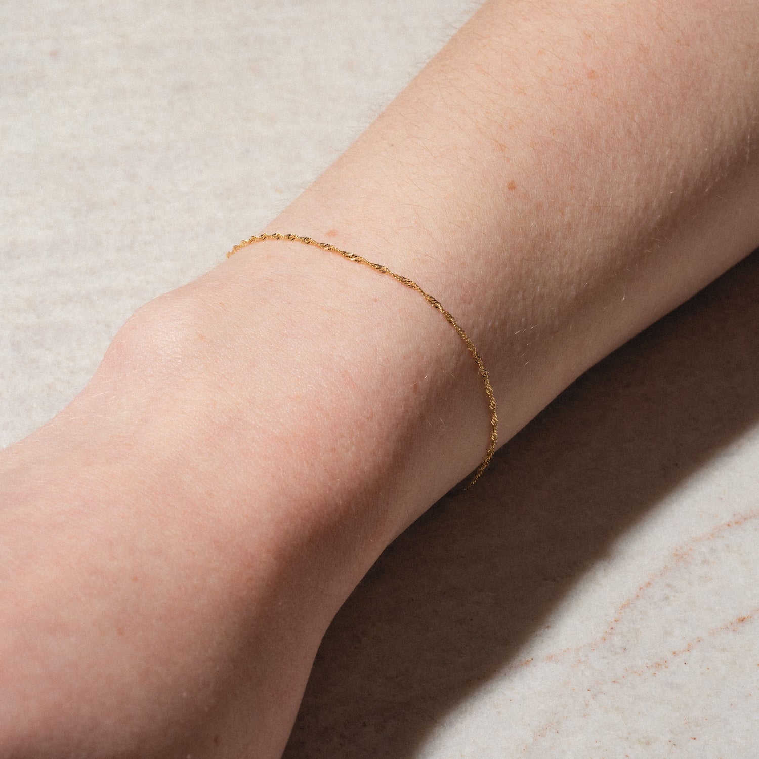 The Solid Gold Twisted Chain Bracelet, crafted in 9k gold, is elegantly worn on a wrist and displayed against a neutral, light background.