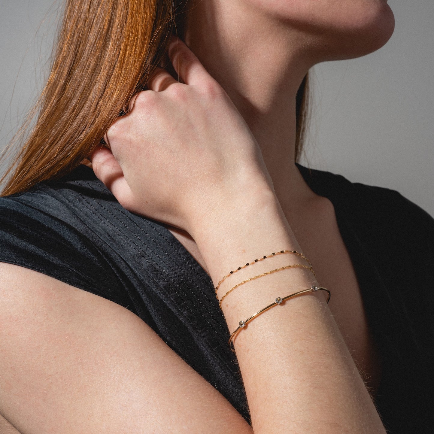 A woman with long red hair, dressed in a black top, poses against a neutral background with her hand touching her hair, showcasing the Solid Gold Bold Sparkle Link Chain Bracelet on her wrist.