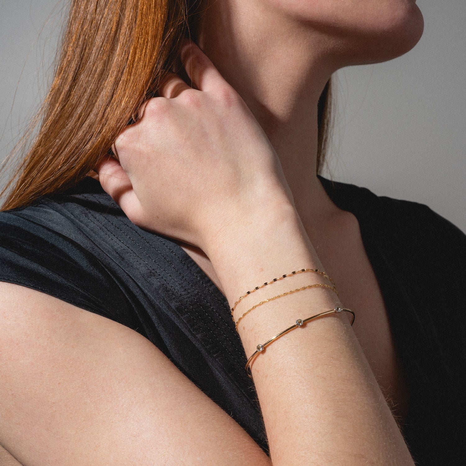 A woman with long red hair, dressed in a black top, poses against a neutral background with her hand touching her hair, showcasing the Solid Gold Bold Sparkle Link Chain Bracelet on her wrist.