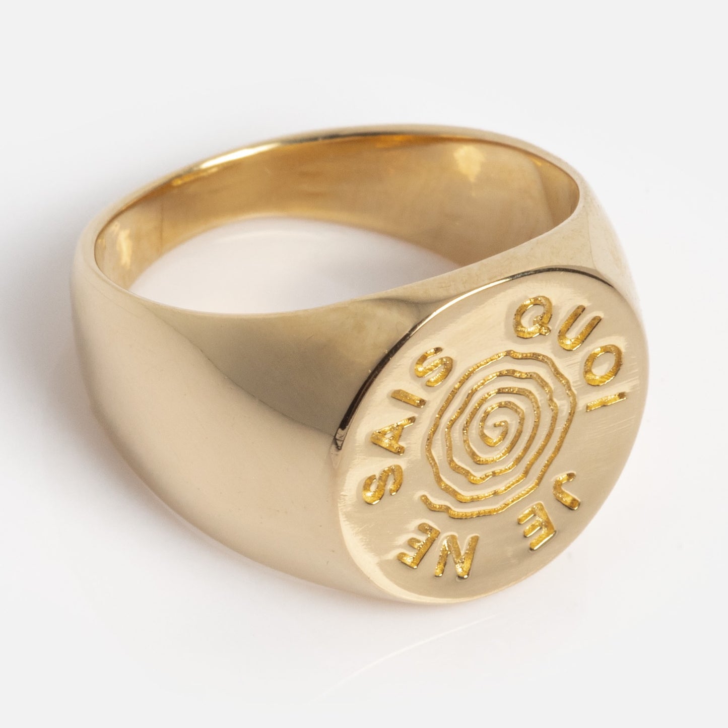 The I Like It Here Club x Local Eclectic Je Ne Sais Quoi Pinky Ring is a gold signet ring with a flat, round top featuring an engraved spiral and the raised words JE NE SAIS QUOI around it.