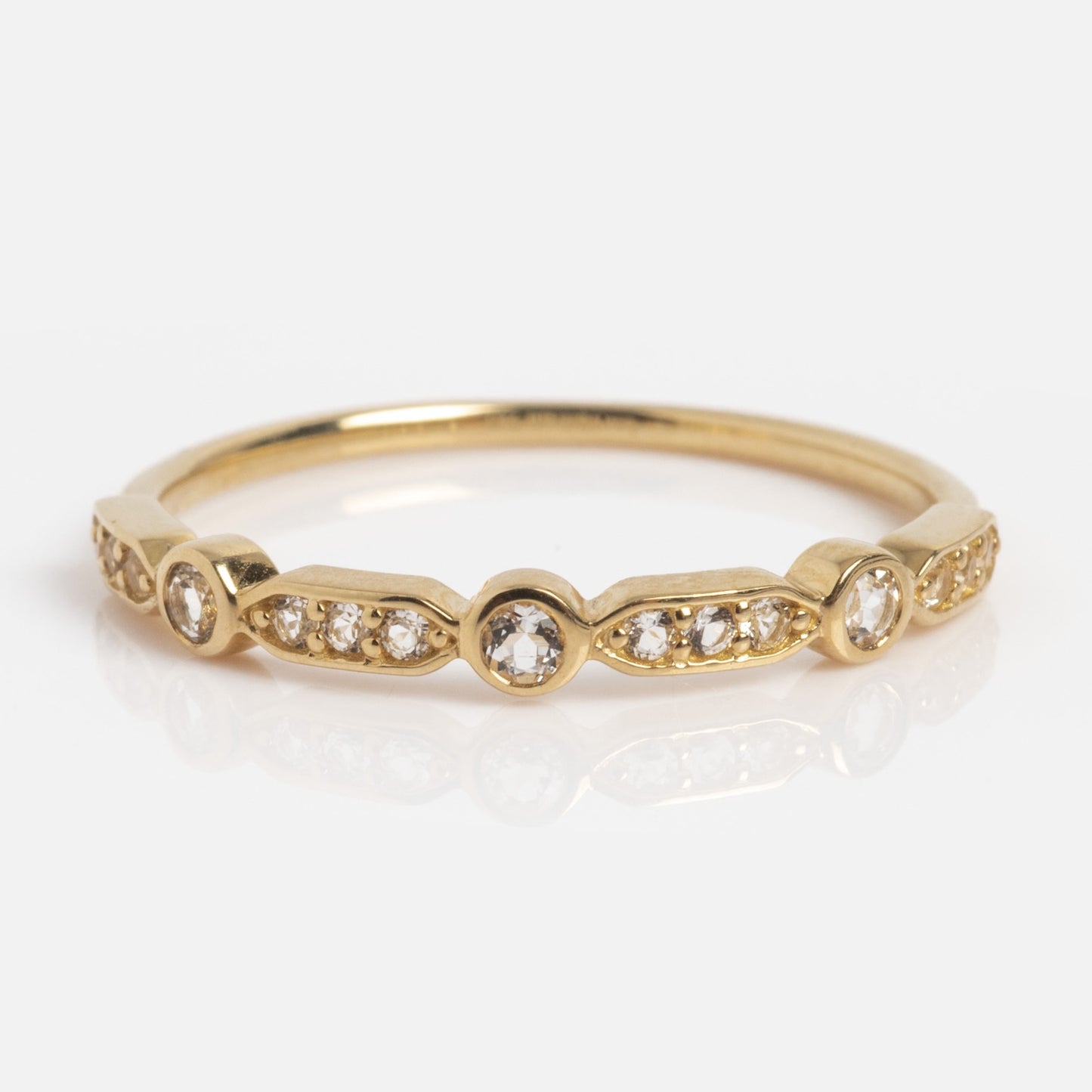 The Solid Gold Bezeled Shimmer Stacking Ring features small round diamonds set in a repeating bezel and pavé pattern along the band, shown against a white background.