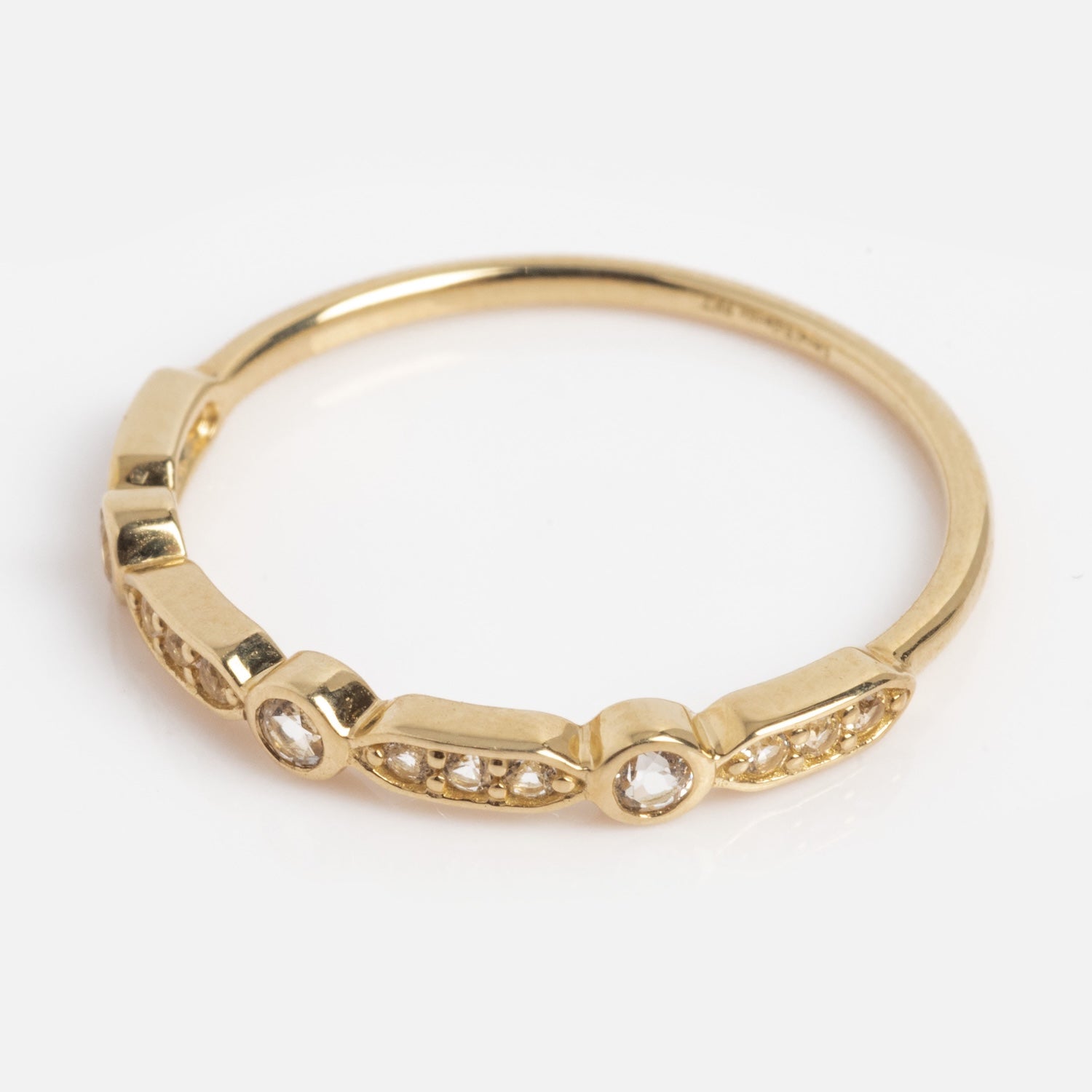The Solid Gold Bezeled Shimmer Stacking Ring is a slim gold band adorned with small, round clear stones in geometric bezels along part of the ring, shown on a white background.