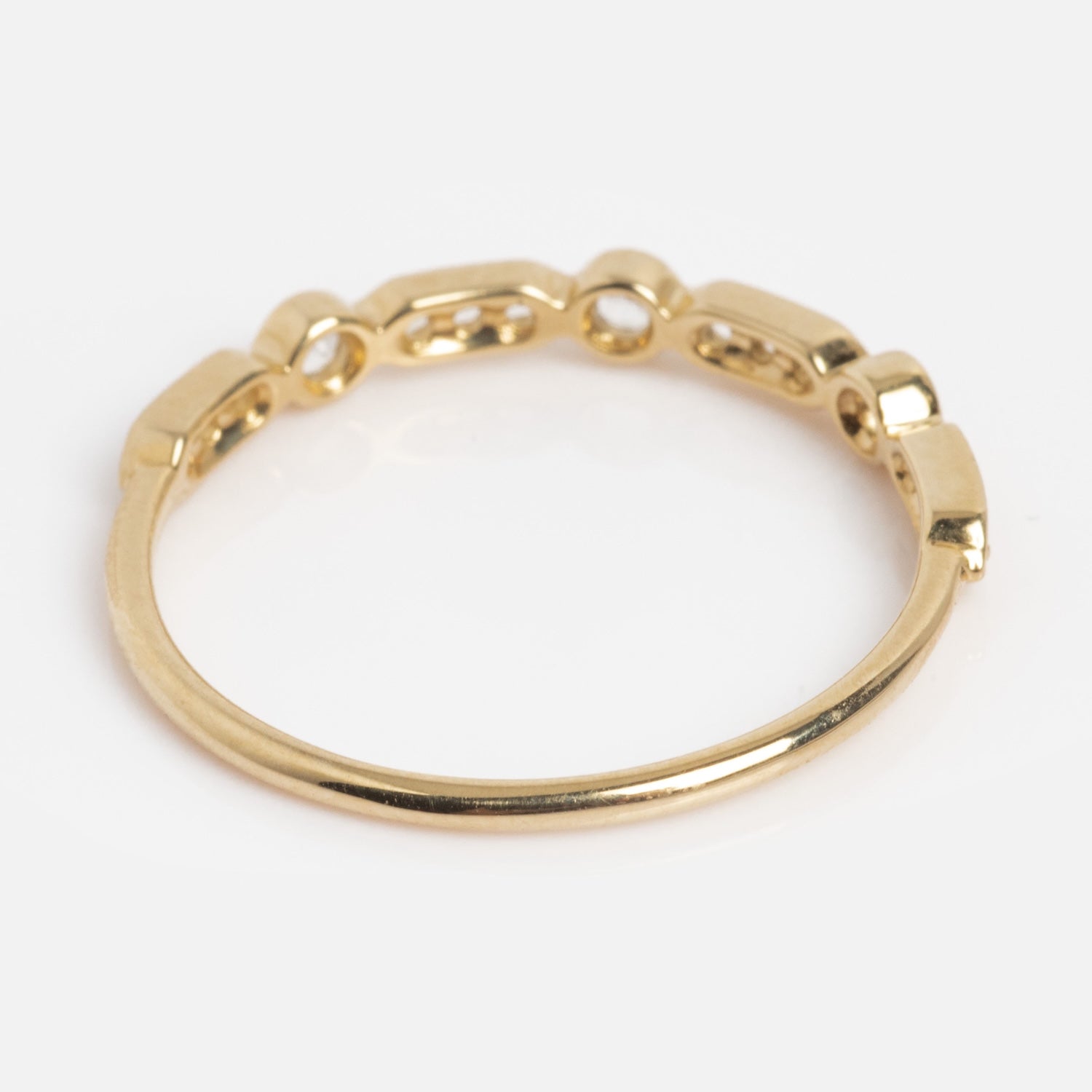 The Solid Gold Bezeled Shimmer Stacking Ring features a smooth gold band in front and small rectangular chain links at the back, beautifully displayed on a plain white background.