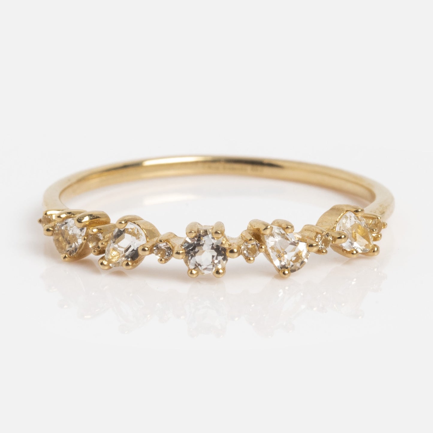 The Solid Gold Floating Gems Stacking Ring showcases five small, uniquely-shaped clear gemstones set in a row on a polished gold band, offering a simple and elegant design.