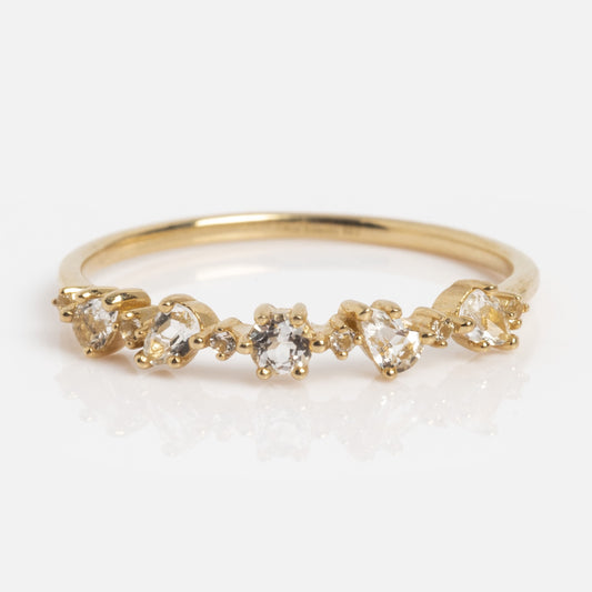 The Solid Gold Floating Gems Stacking Ring showcases five small, uniquely-shaped clear gemstones set in a row on a polished gold band, offering a simple and elegant design.