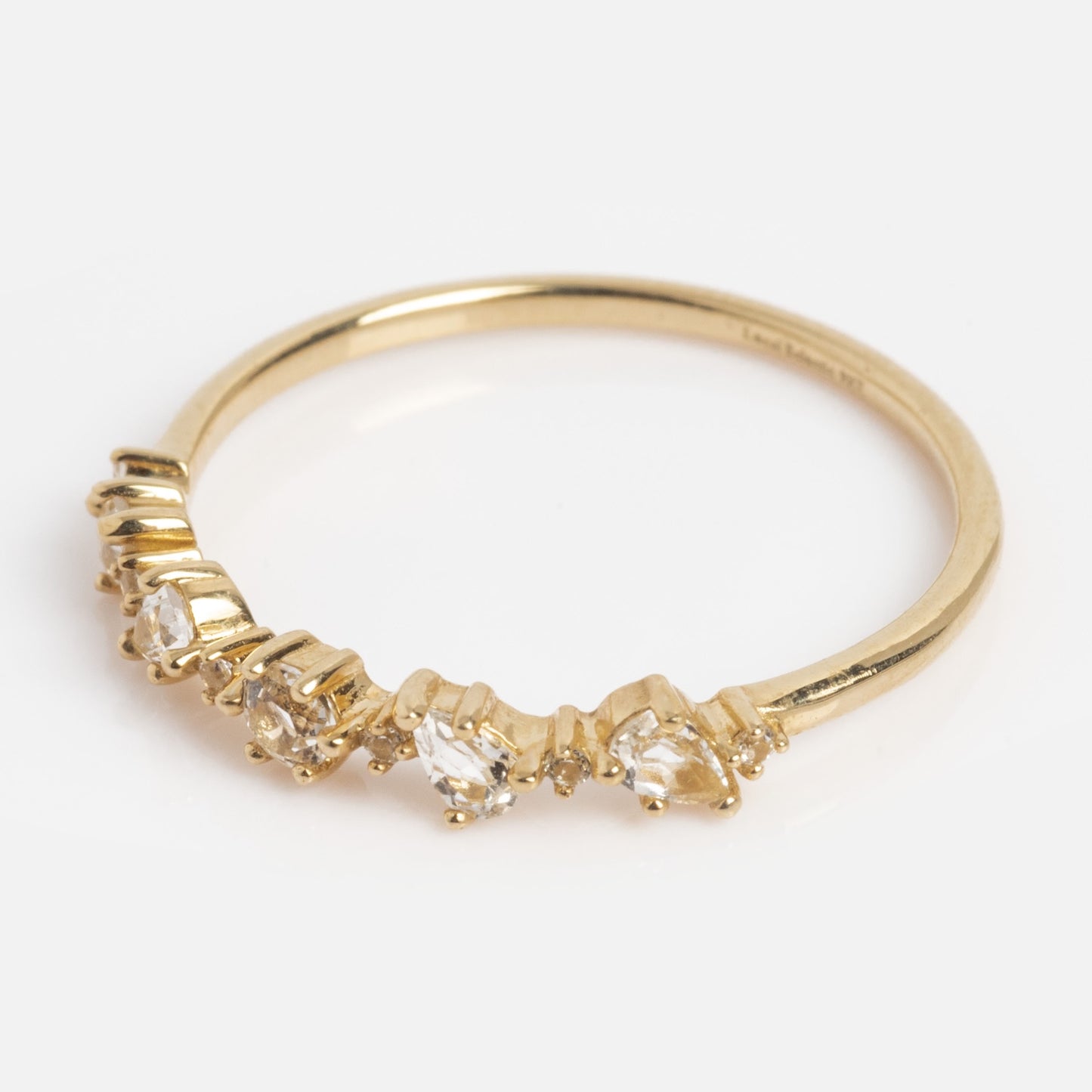 The Solid Gold Floating Gems Stacking Ring features a thin gold band with small clear gemstones set at varying heights on one side, shown against a plain white background.