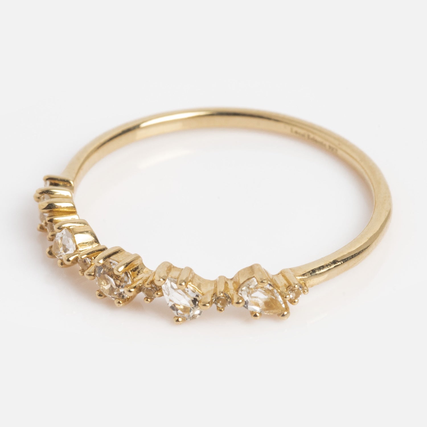 The Solid Gold Floating Gems Stacking Ring features a thin gold band with small clear gemstones set at varying heights on one side, shown against a plain white background.