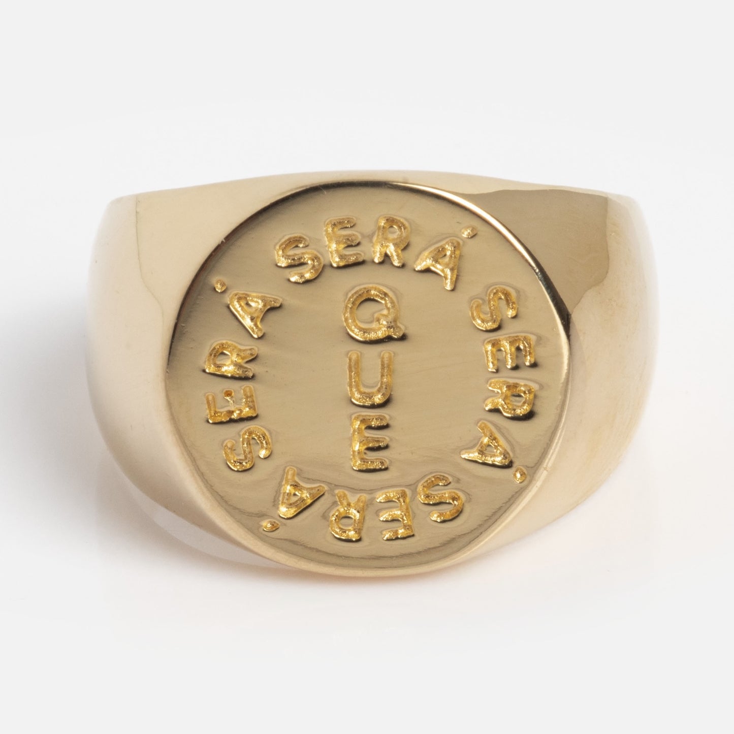 The I Like It Here Club x Local Eclectic Que Sera Sera Pinky Ring is a gold ring with a round face engraved in raised letters: QUE at the center and SERA SERA SERA SERA encircling it.