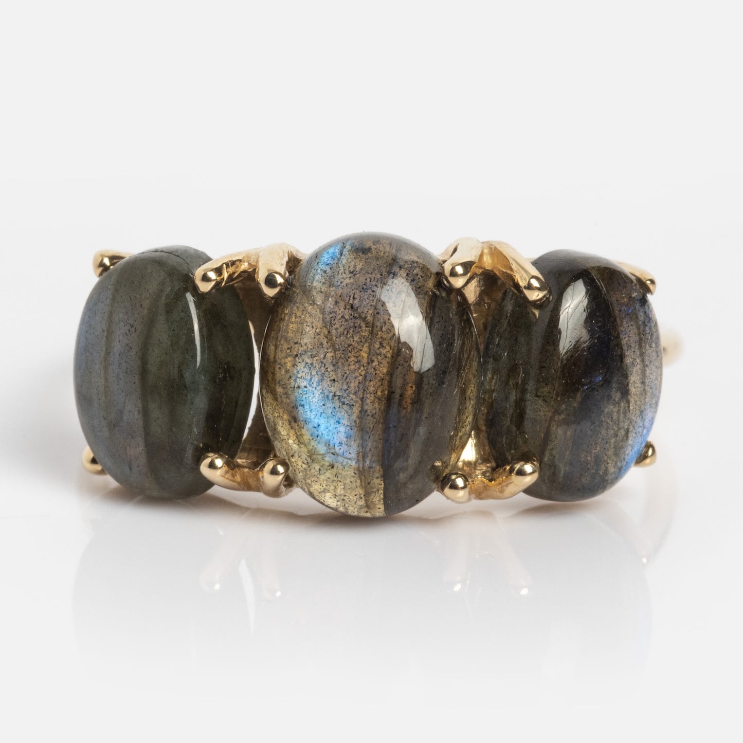 The Sweetest Gumdrop Ring features four oval, polished labradorite gemstones with blue and gold flashes, set in solid yellow gold prongs, arranged in a row against a white background.