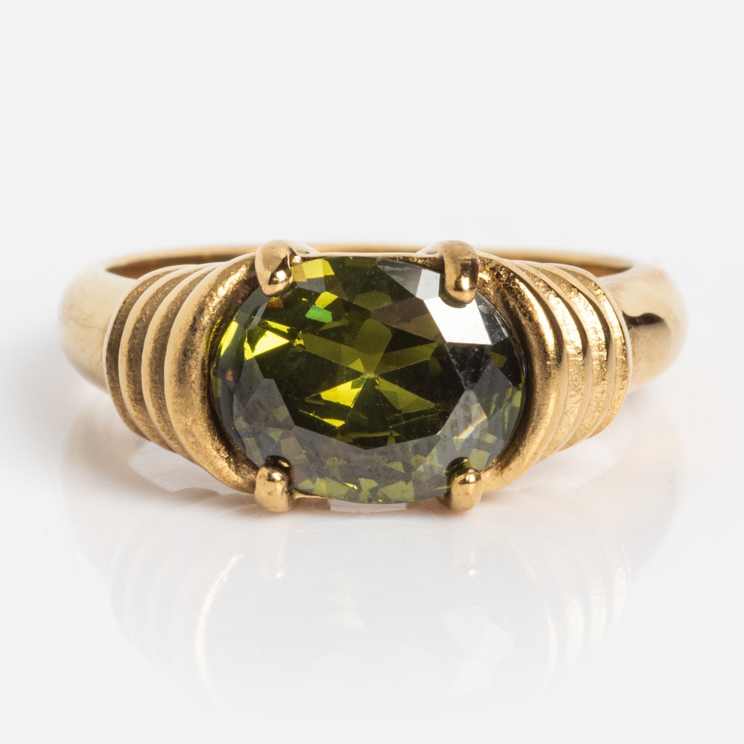 The Stone Statement Ring features a large, round faceted green gemstone at the center, accented by decorative grooved details on each side.