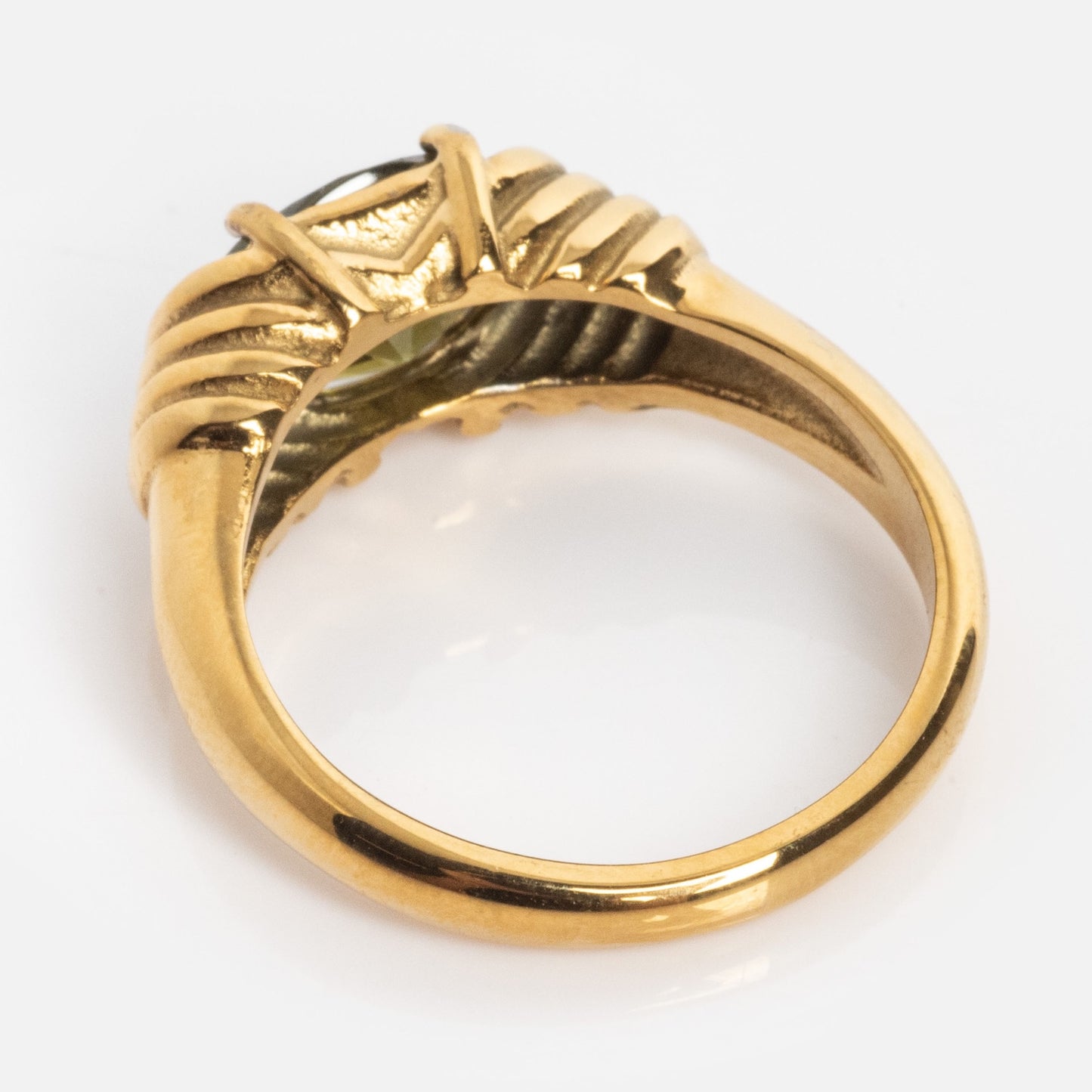 The Stone Statement Ring features a raised, detailed gold setting with ridged, textured elements, shown from an angle that highlights the band and the back of the setting.