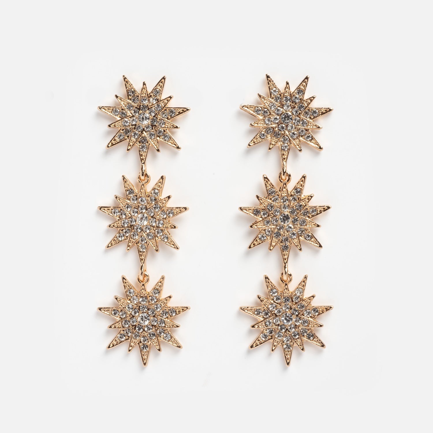 Celestial Drop Earrings in gold-tone, with three sparkling starburst shapes encrusted with clear rhinestones arranged vertically, shown on a plain white background.
