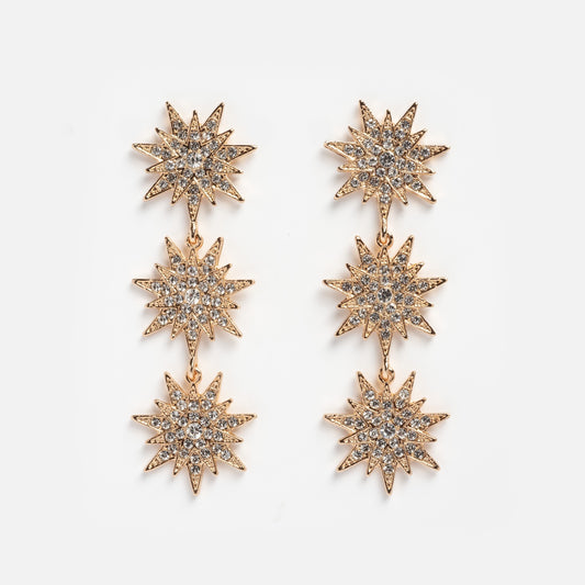 Celestial Drop Earrings in gold-tone, with three sparkling starburst shapes encrusted with clear rhinestones arranged vertically, shown on a plain white background.
