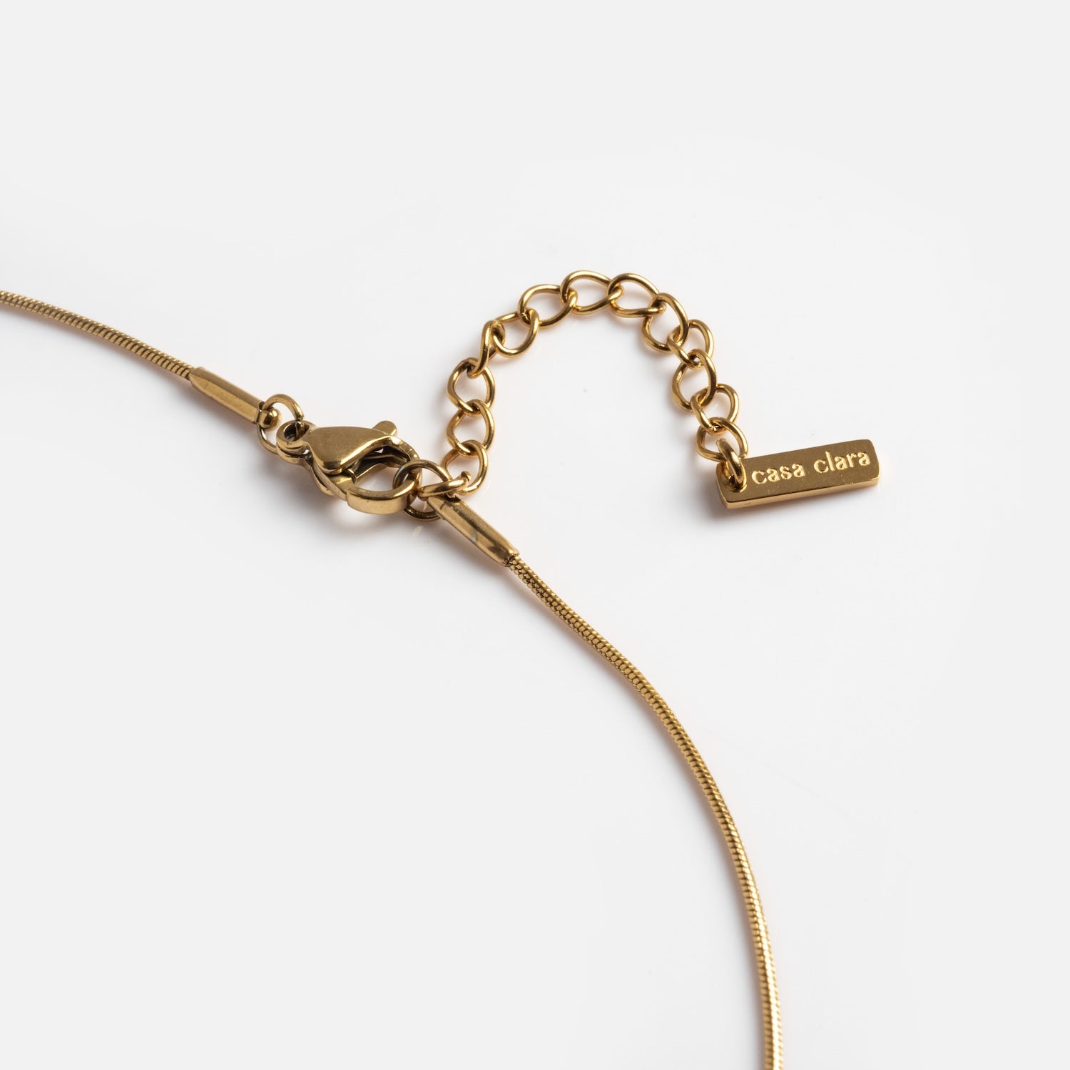 Close-up of the Yellow Necklace with a lobster clasp, extension chain, and a rectangular tag engraved with casa clara at the end. The necklace is shown on a white background.
