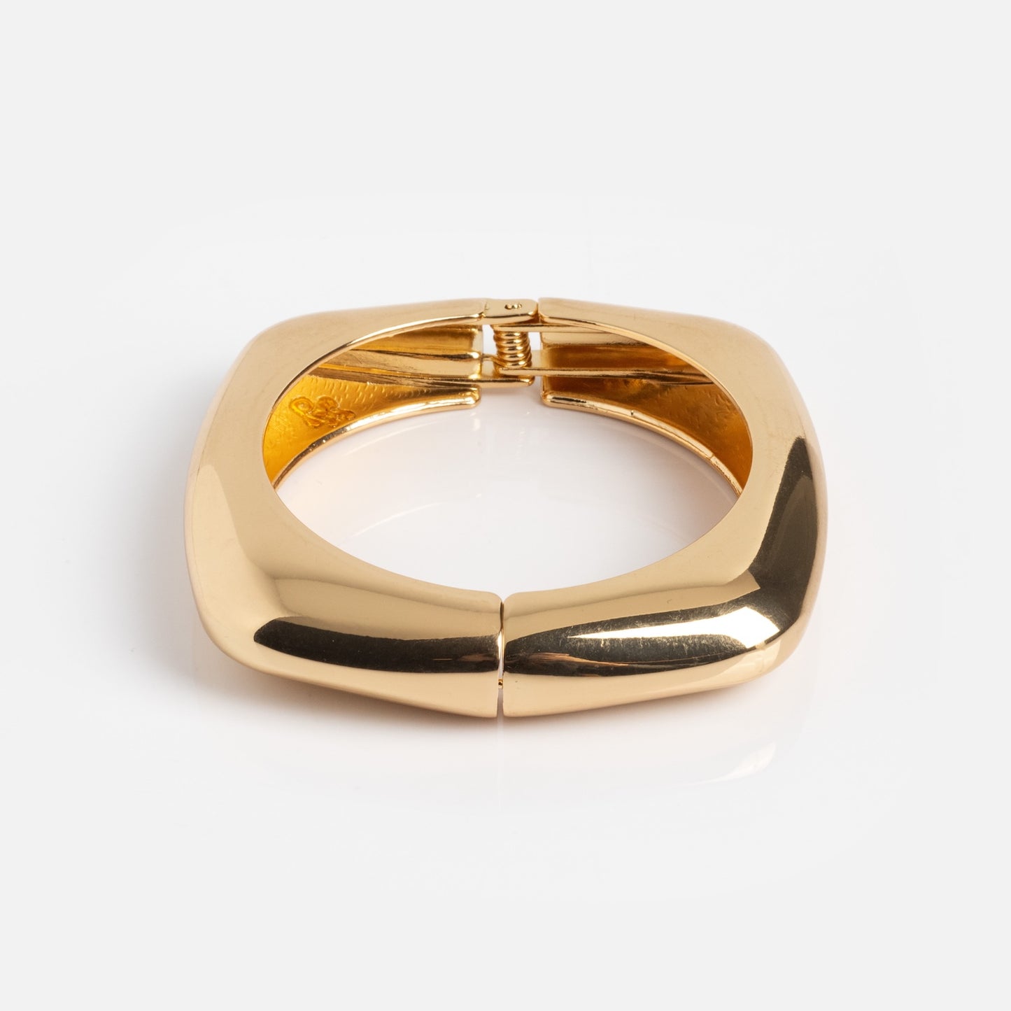 The Square Cuff Bracelet is a chunky, square-shaped gold accessory with smooth, polished surfaces and a hinged clasp, shown against a plain white background.