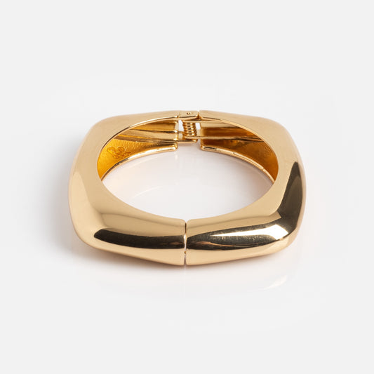 The Square Cuff Bracelet is a chunky, square-shaped gold accessory with smooth, polished surfaces and a hinged clasp, shown against a plain white background.